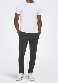 T-shirt en coton blanc associé à un pantalon à rayures grises foncées et des baskets blanches avec des accents verts. Design simple, coupe ajustée.