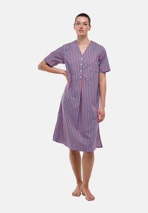 Femme debout pieds nus portant une robe mi-longue à manches courtes avec des rayures verticales rouges, bleues et blanches et des boutons à l'avant.