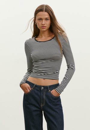 Czarny i biały w paski długi rękaw crop top z okrągłym dekoltem, w zestawieniu z wysokim stanem ciemnoniebieskimi dżinsami z kieszeniami.