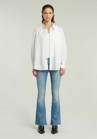 Vit skjorta med lång ärm och tunna ränder, tillsammans med ljusblå utsvängda jeans och svarta ankelstövlar. Slät tygkvalitet.