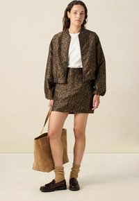 Veste bomber à imprimé léopard et mini-jupe en tons bruns, associées à un haut blanc, des mocassins épais et un sac fourre-tout en daim beige.