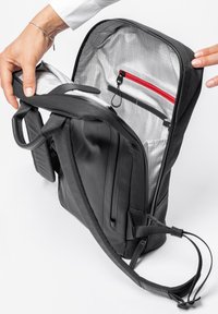 Zaino nero dalla forma rettangolare, con un scomparto zip, interno grigio con motivo a griglia e una tasca zip rossa.