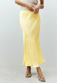 Jupe maxi en satin jaune avec une silhouette fluides, une texture lisse et un léger éclat, associée à des sandales à lanières neutres.