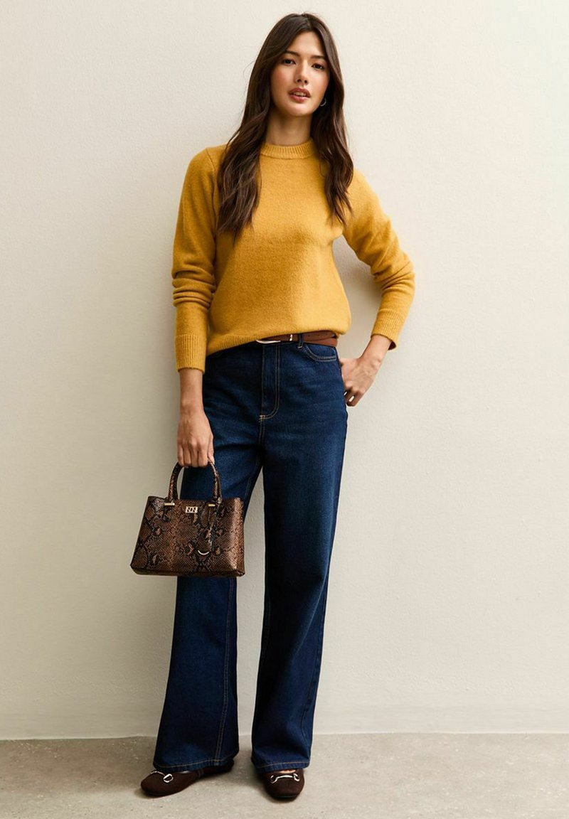 Geel gebreid sweater, donkerblauwe wijde jeans, bruine handtas met slangenpatroon en bruine platte schoenen met accenten. Eenvoudig, getextureerd ontwerp.