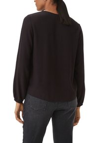 Black long-sleeve blouse with a rounded neckline and gathered sleeves. Paired with dark gray fitted jeans, featuring back pockets.