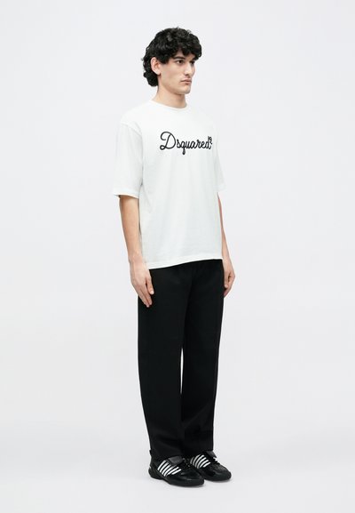 White short-sleeve t-shirt with black cursive "Dsquared2" logo, worn with black trousers and black shoes featuring white stripes.