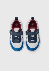 Zapatillas deportivas de malla blanca con acentos en azul marino y rojo, correa ajustable y suelas texturizadas. La etiqueta de tamaño en el interior muestra '24'.