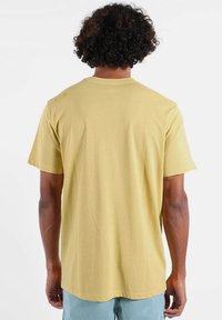 T-shirt jaune manches courtes en coton, avec un col rond et un design simple. La vue de dos montre une texture lisse et des lignes épurées.