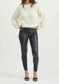 Suéter blanco de punto con hombros caídos y ribete de canalé, combinado con leggings ajustados de imitación cuero negro y tacones abiertos negros.