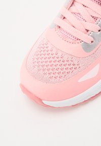 Pink athletic shoe featuring a mesh upper, textured surface, silver accents, and a white sole. Laces are also pink with a subtle sheen.