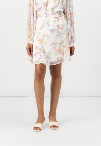Robe florale avec un fond blanc, ornée de fleurs orange, violettes et vertes. Taille élastique, tissu doux, longueur au genou, ourlet froncé.