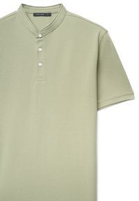 Polo verde a maniche corte con colletto alto, caratterizzata da tre bottoni bianchi, tessuto strutturato e orlo dritto. Etichetta del marchio visibile.