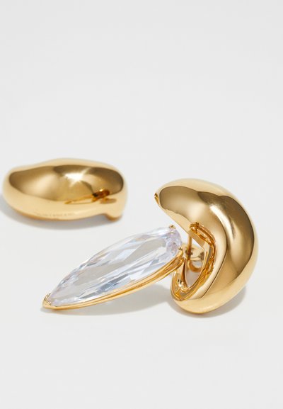 Goldfarbene Ohrringe mit einem glatten, runden Design und einem zentralen, marquise-förmigen klaren Edelstein. Polierte Metalloberfläche, modernes Äußeres.
