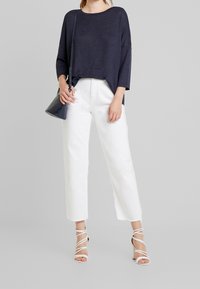 Marinblå oversize stickad tröja, vita vida byxor och vit sandaler med remmar och klack. Accessoar: liten svart handväska med axelrem.