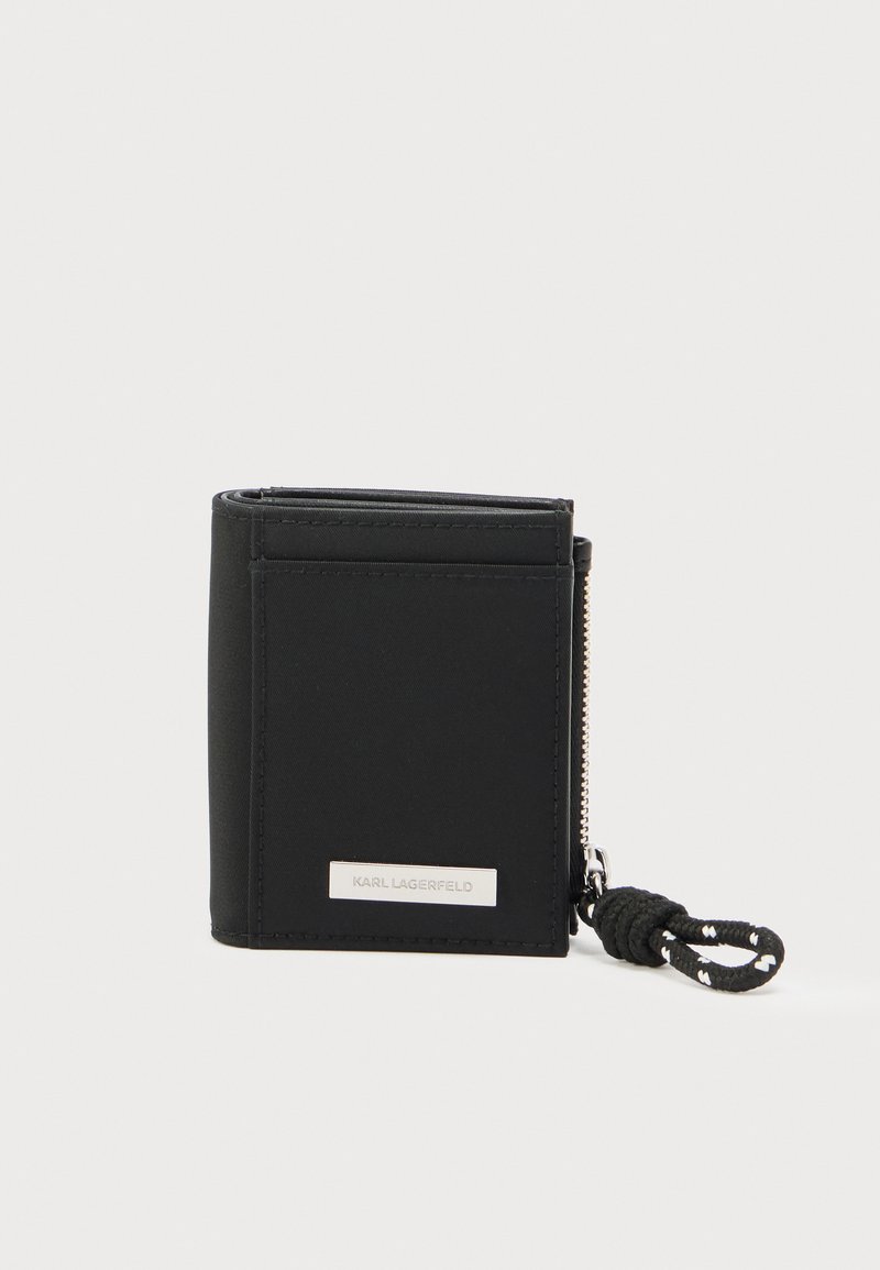 Μαύρο πορτοφόλι από νάιλον με φερμουάρ, με ασημένια πλακέτα λογότυπου και υφασμένο ιμάντα με υφή. Συμπαγής, ορθογώνιος σχεδιασμός.