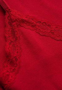 Tissu rouge côtelé avec une bande diagonale de dentelle florale rouge créant un contraste de texture et de motif.