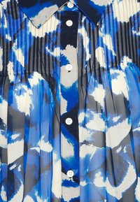 Blau-weiß gemustertes Hemd mit Knöpfen und Falten, mit klassischem Kragen und fünf weißen Knöpfen auf navyblauem Hintergrund.
