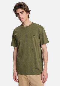 Olive green t-shirt made of textured cotton, featuring a crew neck, short sleeves, and a small black logo on the left chest.