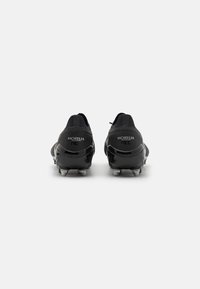 Scarpini da calcio neri con tomaia in pelle liscia, leggero lucido, colletto imbottito e tacchetti metallici sulla suola; il testo "MORELIA" è visibile.