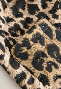 Tikkeline kangas leopardimustriga, millel on mustad täpid beežil taustal, nähtava õmblemise detailiga ja pehme tekstuuriga.