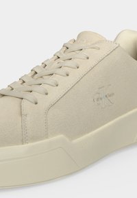 Baskets Calvin Klein en daim beige avec lacets assortis et une semelle épaisse, affichant le logo de la marque en relief sur le côté.