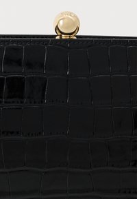 Μαύρη παλαιωμένη δερμάτινη τσάντα με υφή κροκόδειλου, διαθέτοντας στρογγυλεμένο χρυσό κλείσιμο στην κορυφή, που επιδεικνύει μια δομημένη σχεδίαση.