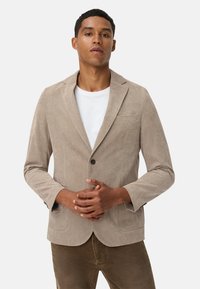 Hellbeige Cordjacke aus Cord mit einem einzigen Knopfverschluss, mit Reverskragen und zwei vorderen Taschen, kombiniert mit einem weißen T-Shirt.