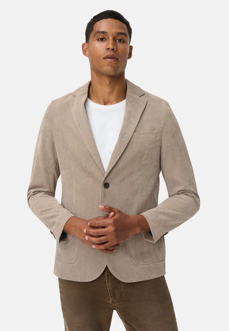 Hellbeige Cordjacke aus Cord mit einem einzigen Knopfverschluss, mit Reverskragen und zwei vorderen Taschen, kombiniert mit einem weißen T-Shirt.