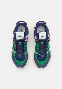 Une paire de baskets Lacoste colorées avec des accents bleu marine, vert, rose et beige, des semelles blanches et des logos de crocodile verts sur les languettes.