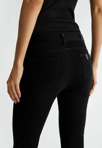 Jeans in denim nero con un design aderente, stile a cinque tasche e dettagli di cucitura sottili. Il tessuto ha una consistenza liscia e leggermente elastica.