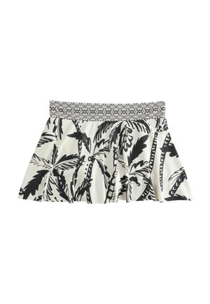 Woman wearing a black and white tropical print skirt and matching top, showing midriff and toned legs against a neutral background.