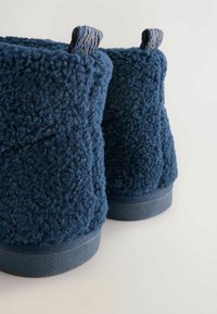 Marineblå ankelstøvler med en tekstureret, fluffy overdel og flade gummisåler. Har løkkede stofdetaljer øverst for nem påtagning.