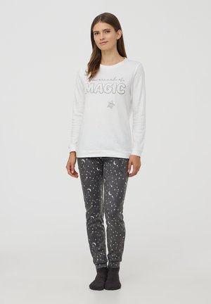 Felpa bianca con la scritta "Sei fatto di... MAGIA" in testo argentato. Pantaloni da pigiama grigi con motivo di lune crescenti e stelle. Tessuto morbido.