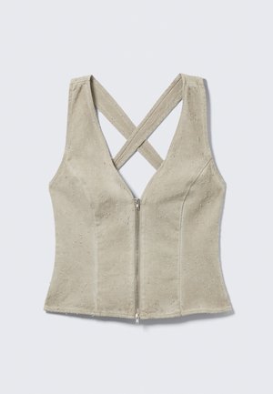 Haut beige sans manches avec une fermeture éclair à l'avant et de larges bretelles croisées dans le dos, fabriqué en tissu texturé.