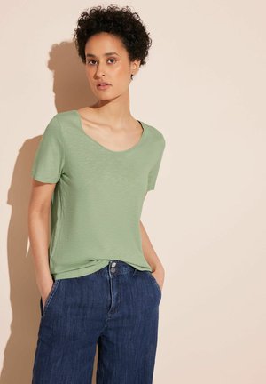 T-shirt verde chiaro a maniche corte con scollatura a barchetta, realizzato in un tessuto testurizzato, abbinato a jeans a gamba larga blu scuro.