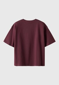 T-shirt en coton bordeaux avec une coupe ample et oversized, des manches courtes et un col rond. Texture lisse, sans motifs ni accents visibles.