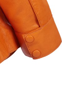 Sleevet på den orange læderjakke har en glat tekstur, synlige syninger og to cirkulære knapper til lukning.
