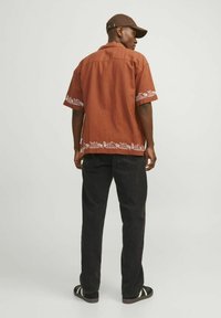 Chemise marron à manches courtes avec broderies florales blanches à l'ourlet, associée à un pantalon noir et des sandales noires avec des rayures blanches.