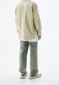 Chemise en velours côtelé beige à manches longues, jeans bleu clair et baskets multicolores avec une semelle texturée. Tissu lisse avec de légères lignes verticales.