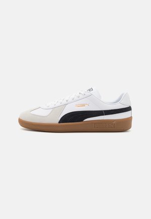 Baskets blanches avec une bande latérale en suede noir, semelle en caoutchouc beige et panneaux texturés. Présente des lacets blancs et des détails avec le logo Puma.