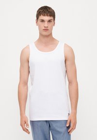 Valge puuvillane tank top ümmarguse kaeluse ja laia käeauguga. Omab õrna tekstuuriga mustrit ja väikest musta logo allääres.