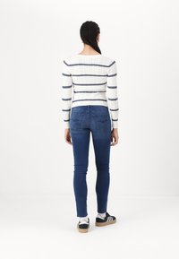 Jersey blanco de punto trenzado con rayas marinas, combinado con unos pantalones vaqueros ajustados azules y zapatillas negras. La vestimenta se ve desde la parte posterior.
