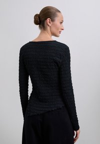 Zwarte langetermijnsleeve shirt van een gestructureerde, gekreukte stof. Heeft een brede hals en een licht gebogen zoom aan de achterkant.