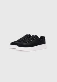 Black sneakers with suede and smooth textile upper, round toe, flat white rubber sole, and black laces. Features logo on tongue.