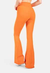 Rozszerzane legginsy do jogi w jasnym pomarańczowym kolorze. Wykonane z elastycznej tkaniny o gładkiej fakturze, z wysokim stanem i dopasowanym krojem.