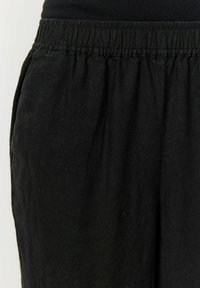 Svarta linnebyxor med elastisk midja, strukturerad tyg och veckdetalj framtill. Inga synliga fickor eller metalldetaljer.