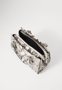 Tekstureret taske med slangeprint i hvid og sort med sølvfarvet hardware, dobbelte lynlåse og dekorative detaljer. Åbnet for at afsløre en sort inderside.