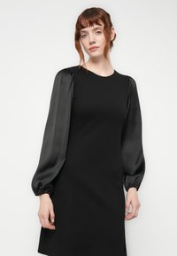 Black dress with a fitted silhouette, featuring long satin puff sleeves and a round neckline; smooth texture with elastic cuffs.