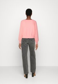 Heller rosa, gekürzter Pullover mit weicher Textur, kombiniert mit hochgeschnittenen, dunkelgrauen Jeans, die dezente Gesäßtaschen und eine lockere Passform haben.