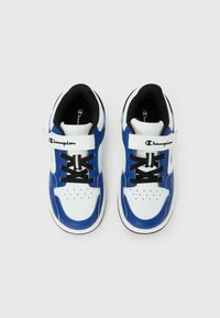 Άσπρα και μπλε αθλητικά παπούτσια Champion με μαύρα κορδόνια και λουράκι με βέλκρο σε λευκό φόντο, σε θέαση από πάνω.